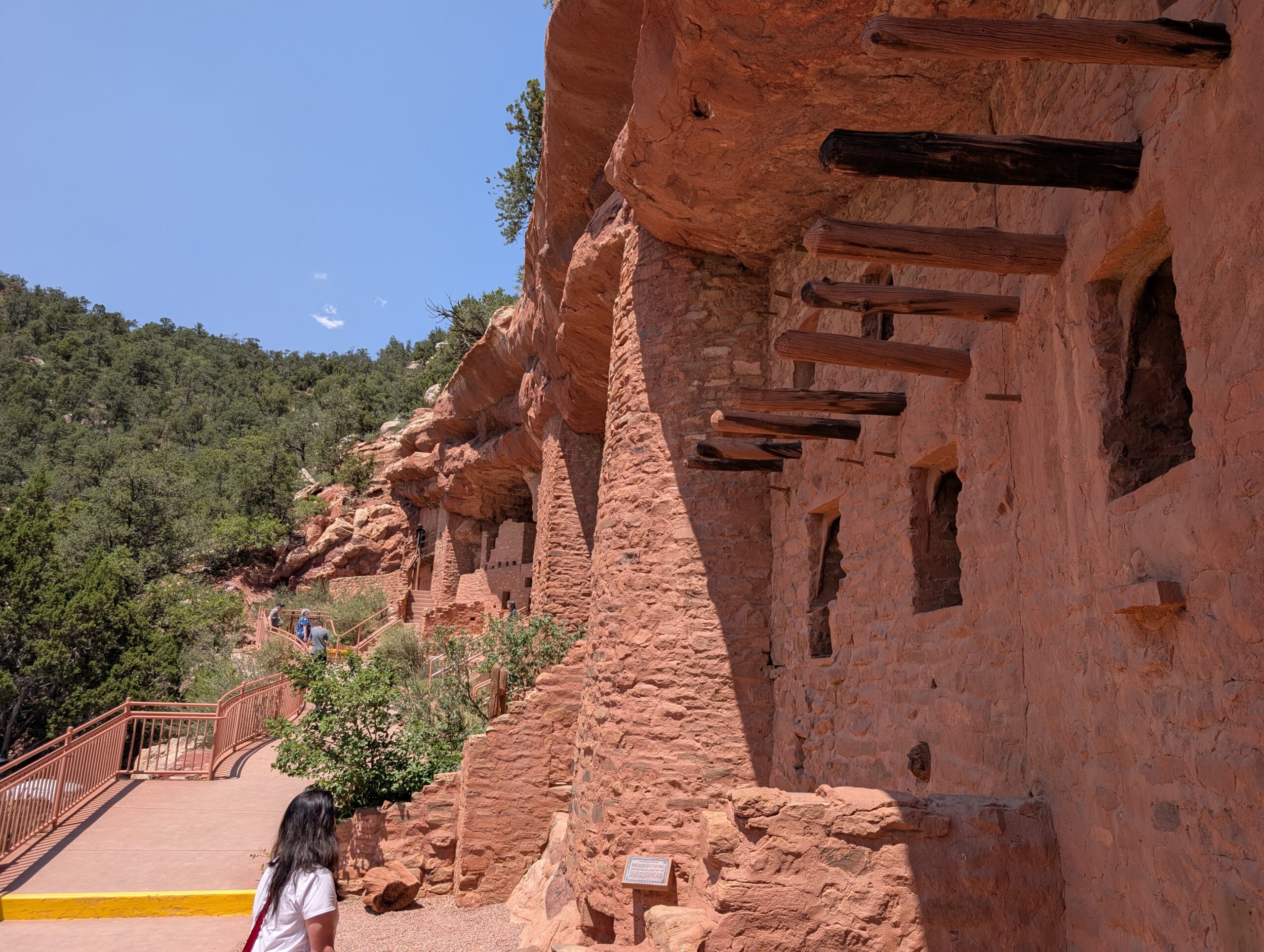 Manitou Cliff Dwellings Visitor walking the boardwalk at the Manitou Cliff Dwellings beneath a red sandstone overhang with original roof timbers