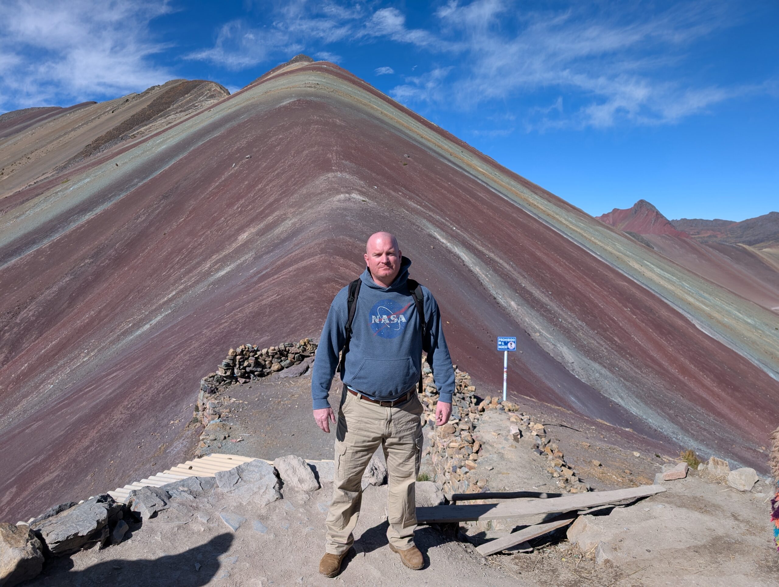 Michael McGill stand at the top of Rainbow mountain in a NASA hoodie