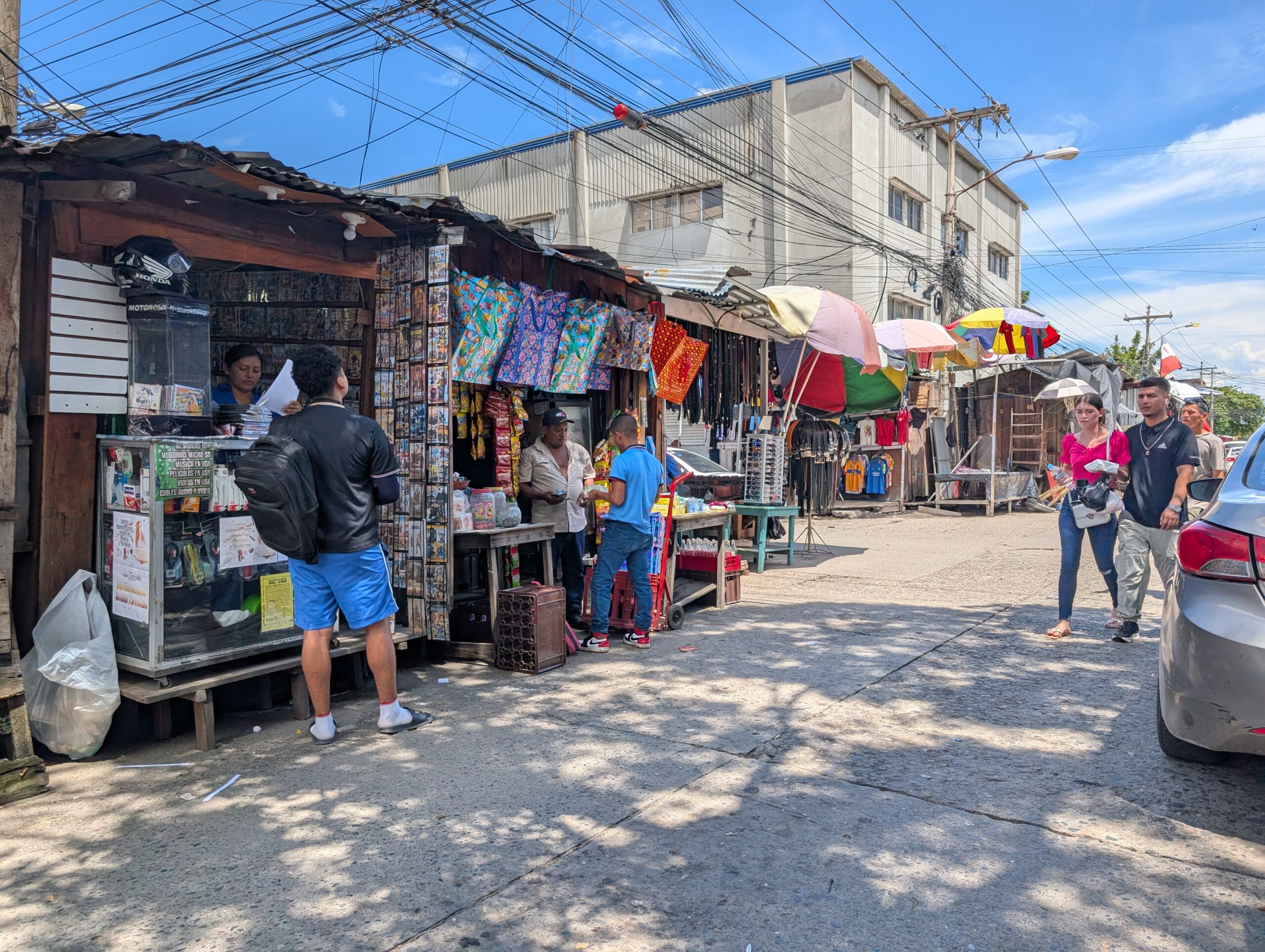 San Pedro Sula Street Vendors Wooden street stalls selling DVDs, snacks, bags, and belts under tangled power lines in downtown San Pedro Sula, Honduras.